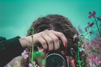 selective focus of woman behind pink flowers holding red Samsung bridge camera about to take photo of flower